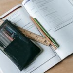 From above of textbook with exercises and ruler with pens near small case on table